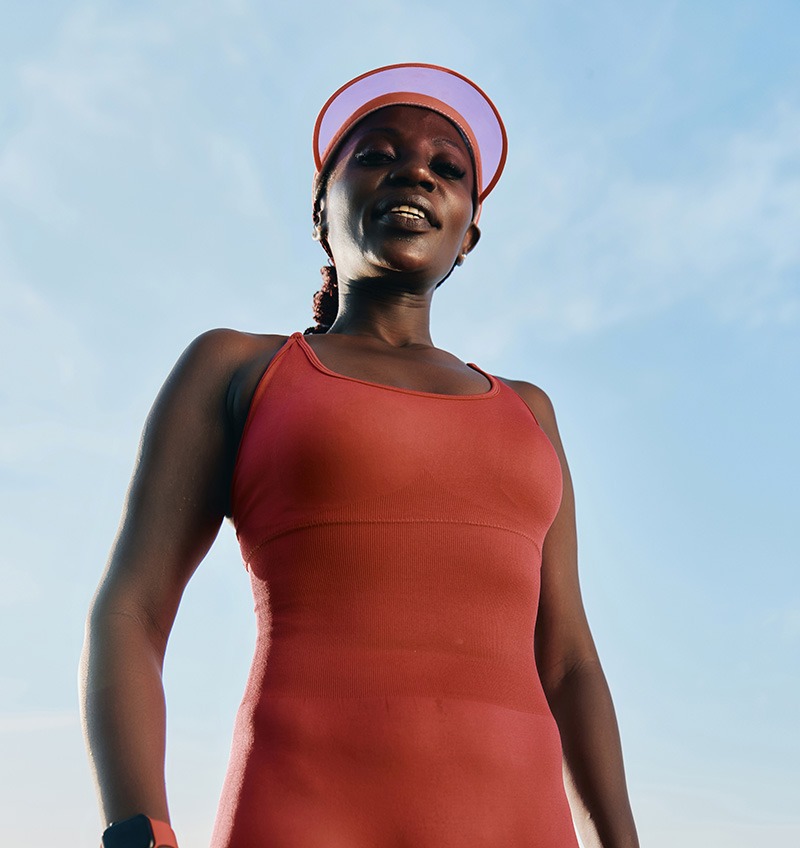 Woman in a red athletic outfit and visor standing outdoors, looking confidently at the camera with a blue sky in the background.