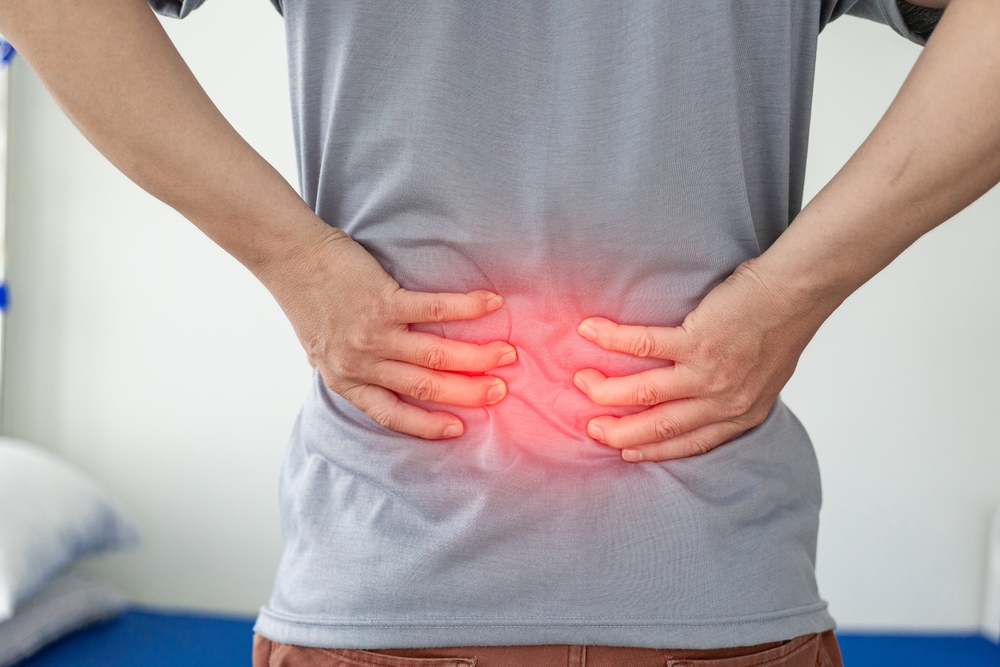 A person holding their lower back with both hands, with a red highlighted area indicating pain or discomfort in the lower back region.